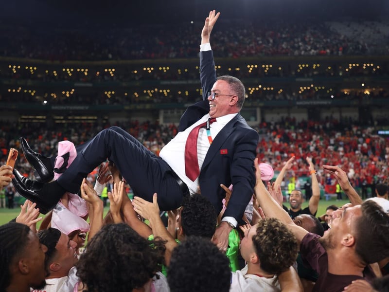 Fouzi Lekjaa, in a suit, tossed in the air by Morocco's players on the pitch after the win over the Netherlands