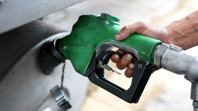 A hand holds a green fuel pump nozzle inserted in a vehicle's fuel tank