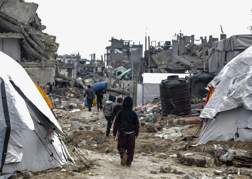 Children walk between tents and rubble in Jabalia camp in the Gaza Strip, past a black water tank and collapsed buildings