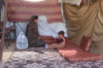 A mother sits with her young child on a mattress inside a tent at a displacement site in Deir al Balah, Gaza