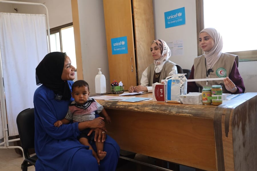 A mother holds her infant at a UNICEF-supported breastfeeding counselling session with two health workers in Gaza