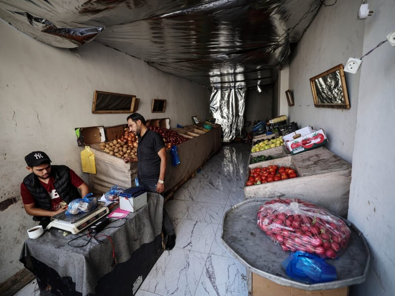Two men in a small vegetable shop in Gaza with crates of onions, potatoes and tomatoes