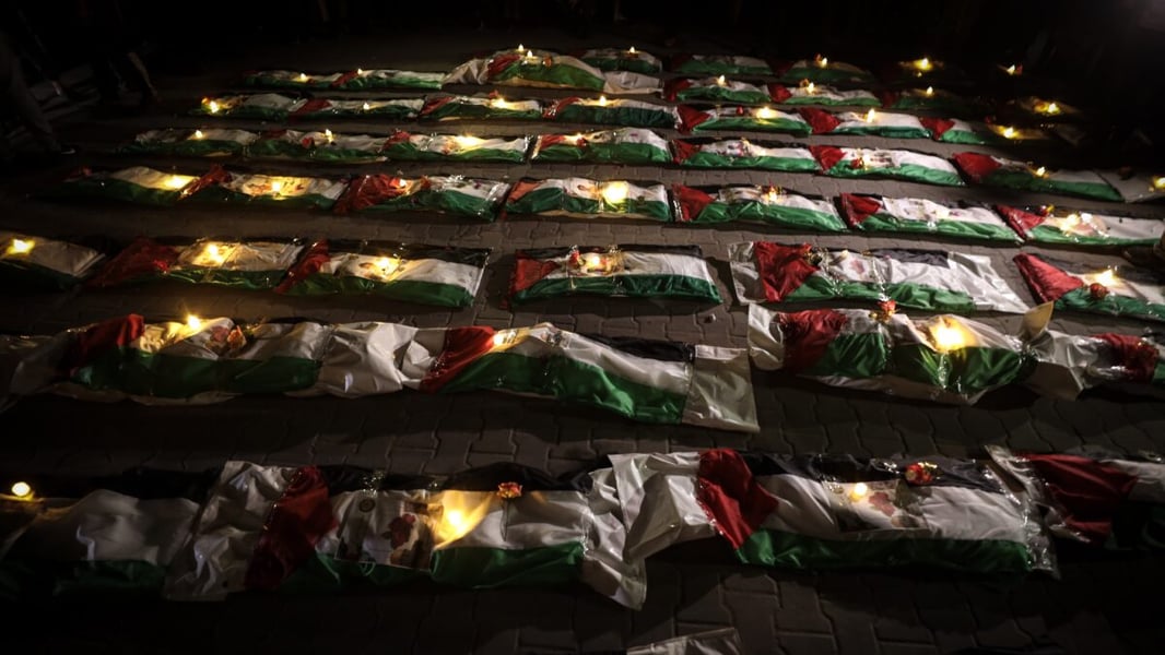 Remains wrapped in Palestinian flags with candles on paving stones at night in Gaza City's Zeitoun neighborhood