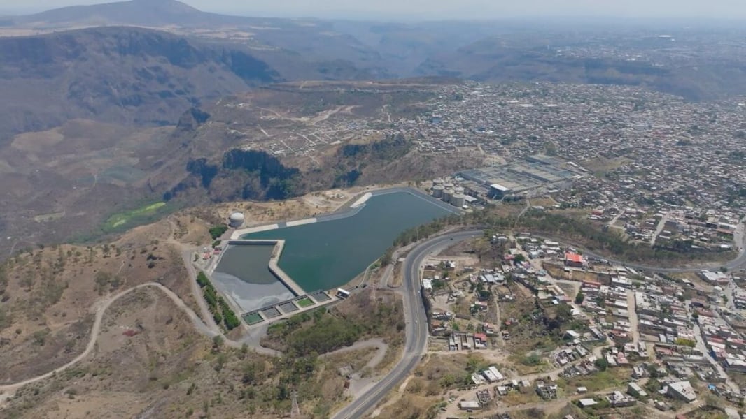 Aerial view of a reservoir and water treatment facilities beside dense residential districts and hills
