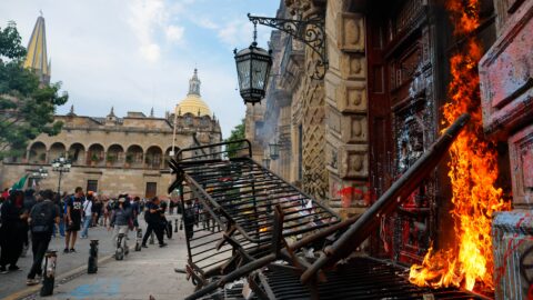 Flames burning at the entrance of a historic building beside a charred metal barrier in central Guadalajara