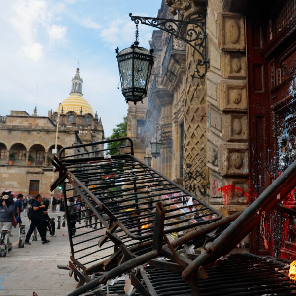 Flames burning at the entrance of a historic building beside a charred metal barrier in central Guadalajara