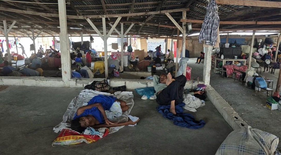 Displaced people lie and sit on the floor of a covered open-sided community space in Port-au-Prince, Haiti