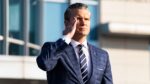 Defense Secretary Pete Hegseth in a plaid suit saluting outside a building