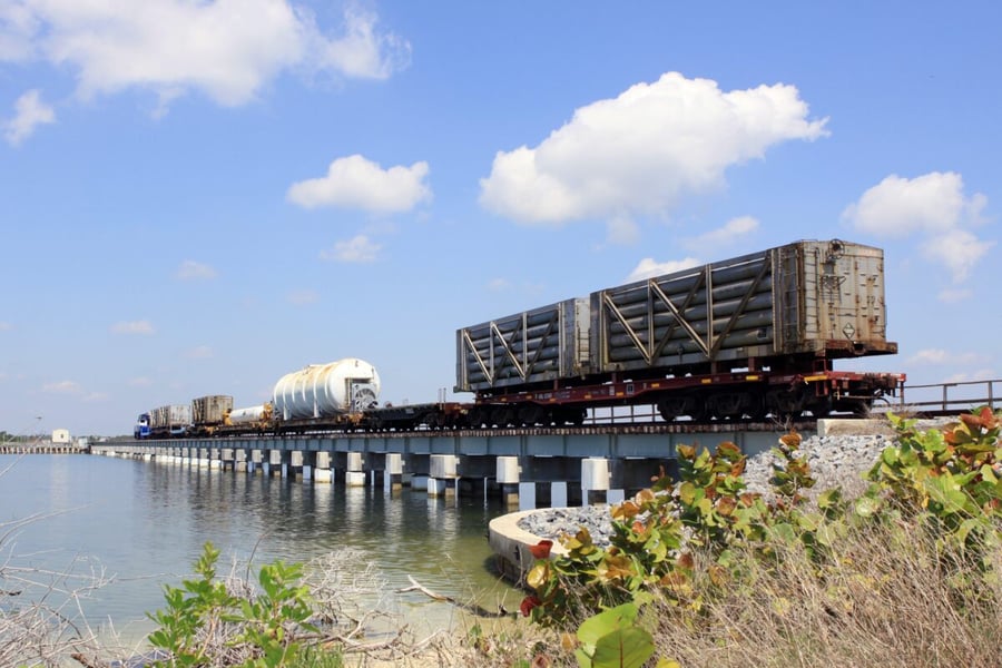 A NASA railroad train with tank cars of helium and other gases crosses a bridge over a Florida waterway under a blue sky