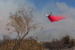 Air tanker drops red fire retardant over smoky hills at Camp Pendleton during the Henderson Fire