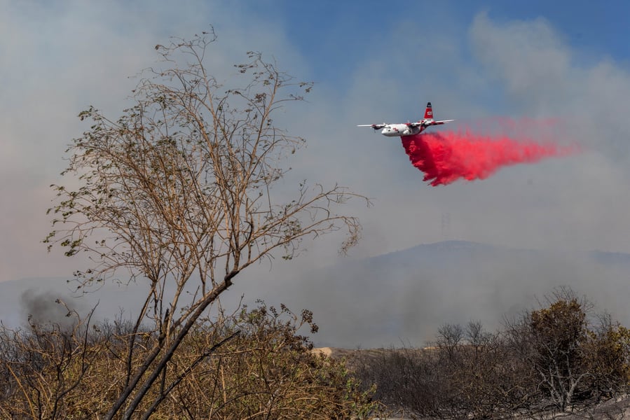 Air tanker drops red fire retardant over smoky hills at Camp Pendleton during the Henderson Fire