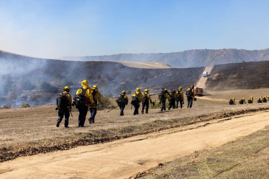 Firefighters walk along a dirt road past smoking hillsides at Camp Pendleton during the Henderson Fire