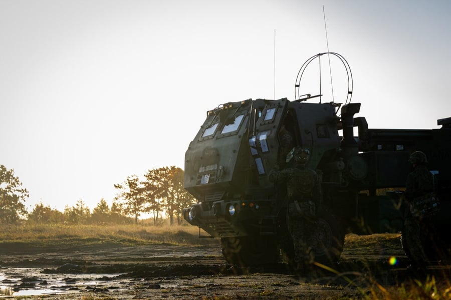 US Marines and a Japanese soldier beside an M142 HIMARS launcher at sunset at the Yausubetsu Training Area in Hokkaido