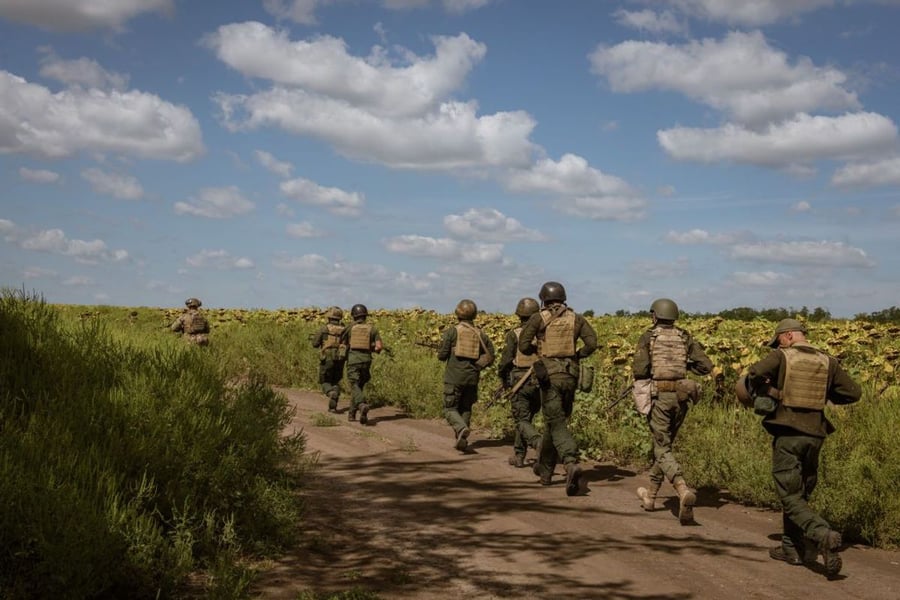 Ukrainian soldiers in body armor and helmets run along a dirt track beside a sunflower field in the Huliaipole district