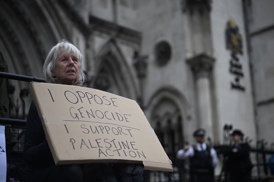A demonstrator holds a cardboard sign reading I oppose genocide, I support Palestine Action, outside the Royal Courts of Justice in London