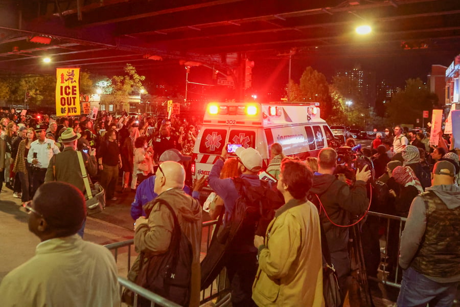 Protesters with an ICE Out of NYC sign crowd a street as an ambulance passes at night after an ICE shooting in New York City