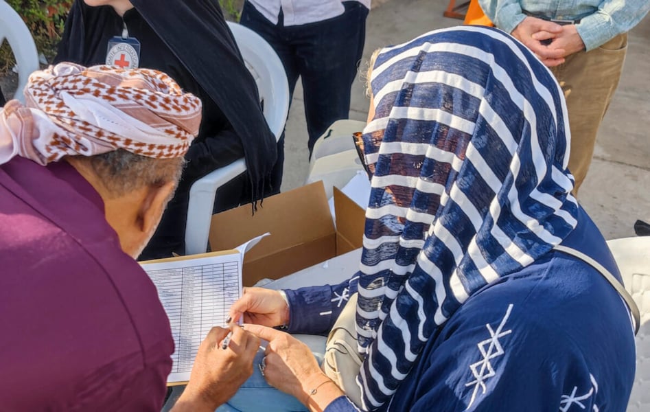 Two people sign a list on a table beside a Red Cross staff member with an ICRC badge during a detainee release in Sanaa