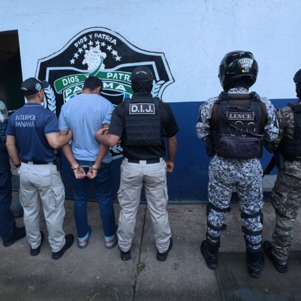 Panamanian police and INTERPOL Panama officers stand with a handcuffed suspect facing a wall during an arrest