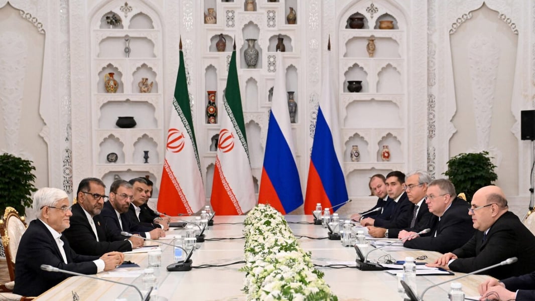 Iranian and Russian delegations seated on opposite sides of a long table with flags behind them