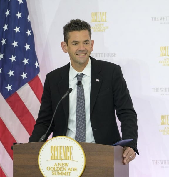 NASA Administrator Jared Isaacman smiles at a podium with the American flag and a Science: A New Golden Age Summit seal