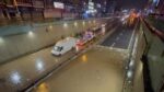 A white van stranded in floodwater on a sunken Istanbul roadway at night as tow trucks and responders gather