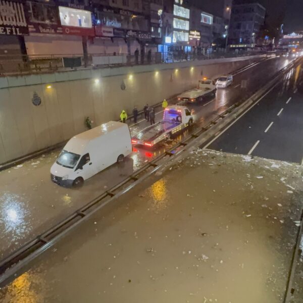 A white van stranded in floodwater on a sunken Istanbul roadway at night as tow trucks and responders gather
