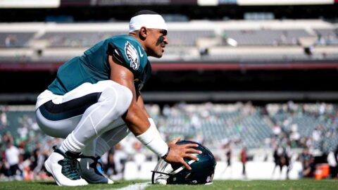 Eagles quarterback Jalen Hurts crouches on the field with his helmet on the grass in a file photo