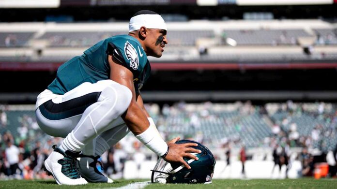 Eagles quarterback Jalen Hurts crouches on the field with his helmet on the grass in a file photo