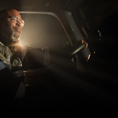 A professional truck driver at the wheel in a dim cab, in an image from J.B. Hunt's website