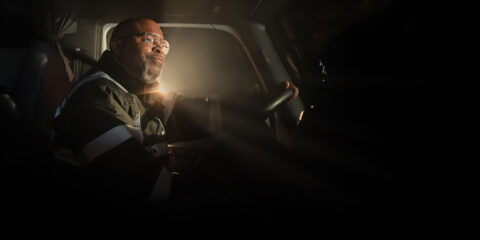 A professional truck driver at the wheel in a dim cab, in an image from J.B. Hunt's website