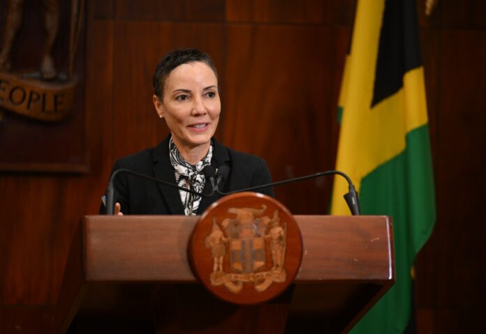 Jamaican Foreign Minister Kamina Johnson Smith speaks at a lectern in front of the Jamaican flag at Jamaica House