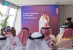 A speaker at a podium during the grand opening ceremony of Lenovo's regional headquarters in Riyadh, with an audience in Saudi headdress in the foreground