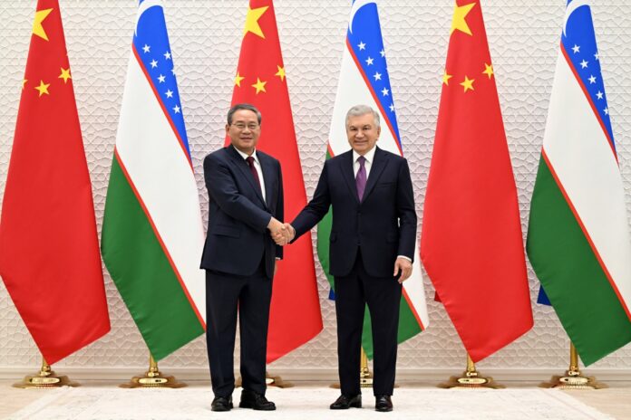 Chinese Premier Li Qiang and Uzbek President Shavkat Mirziyoyev shaking hands in front of Chinese and Uzbek flags