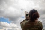 A U.S. Army soldier aims a handheld counter-drone device at a small quadcopter in a cloudy sky during training in Lithuania