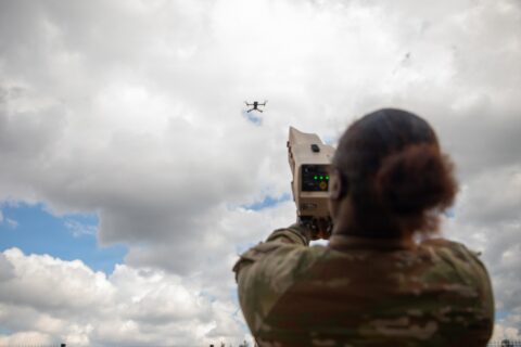 A U.S. Army soldier aims a handheld counter-drone device at a small quadcopter in a cloudy sky during training in Lithuania