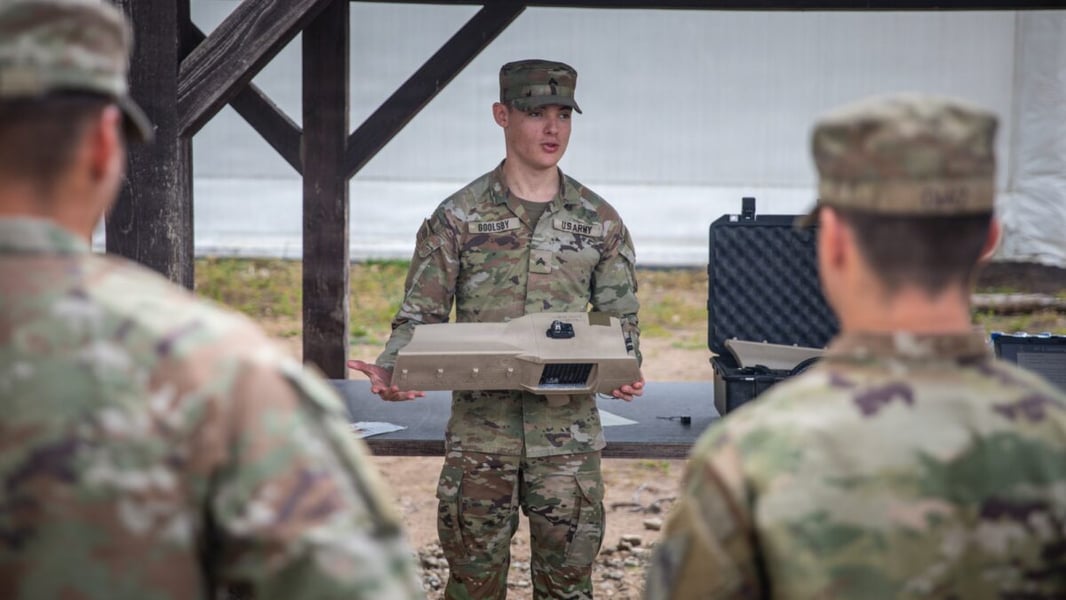 A U.S. Army corporal holds a handheld counter-drone electronic warfare system while briefing soldiers at a training area in Lithuania