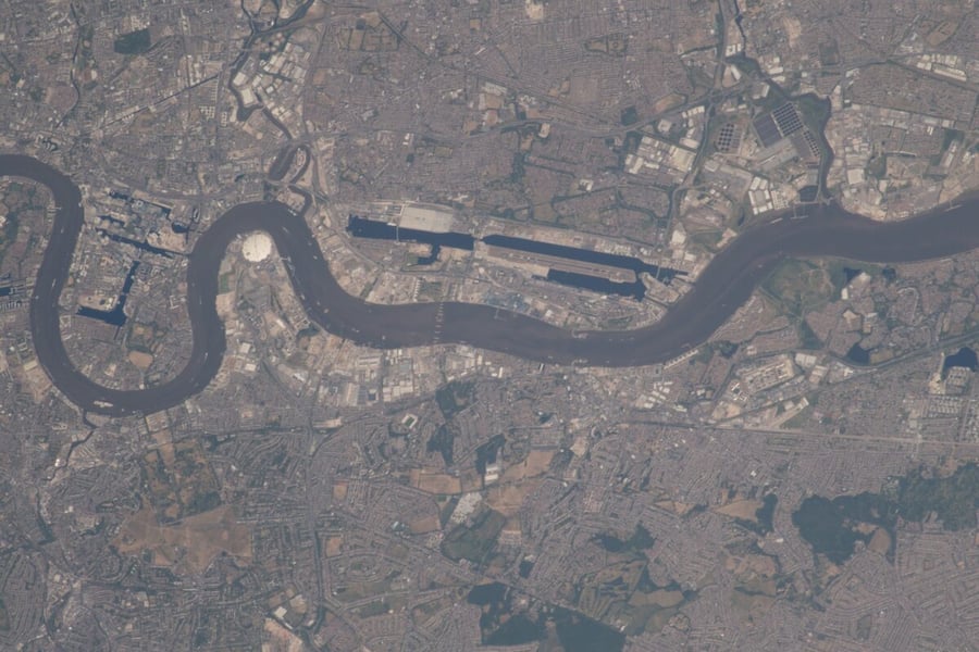 An aerial view from orbit of the River Thames winding through east London past Canary Wharf and London City Airport