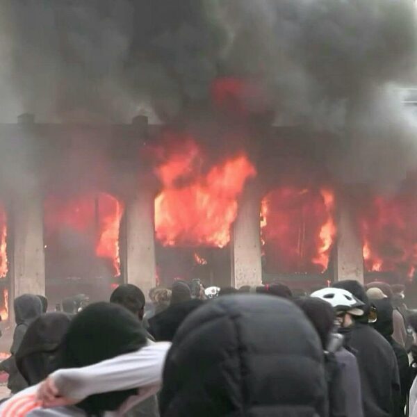 Flames and black smoke pour from the windows of the Lyon tourist office as hooded protesters gather in the square in front