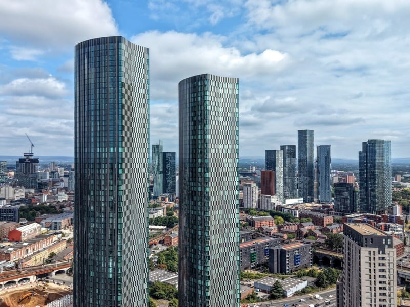 Two glass towers rise above the Manchester skyline on a partly cloudy day
