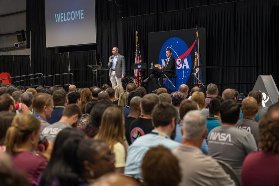 A packed audience of Marshall Space Flight Center employees faces a stage where NASA Administrator Jared Isaacman sits beside a NASA logo backdrop