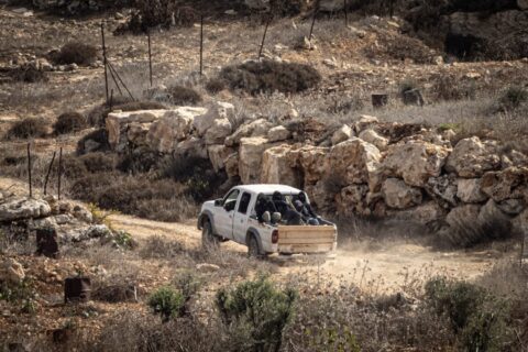 Masked men carrying clubs ride in the back of a white pickup truck on a dirt track in Abu Falah, West Bank