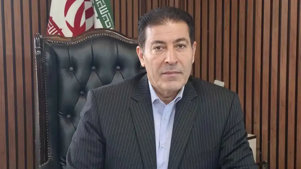 Mehrdad Akhlaghi Ketabchi, in a pinstriped suit seated in front of an Iranian flag, in an undated image