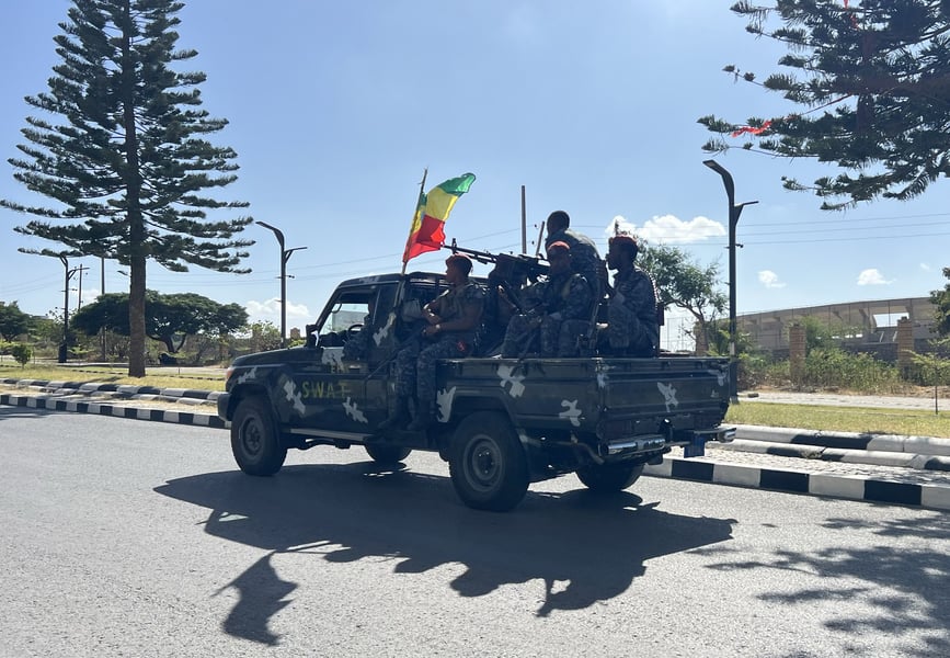 Armed Ethiopian security personnel ride on the back of a pickup truck flying an Ethiopian flag on a road in Mekelle