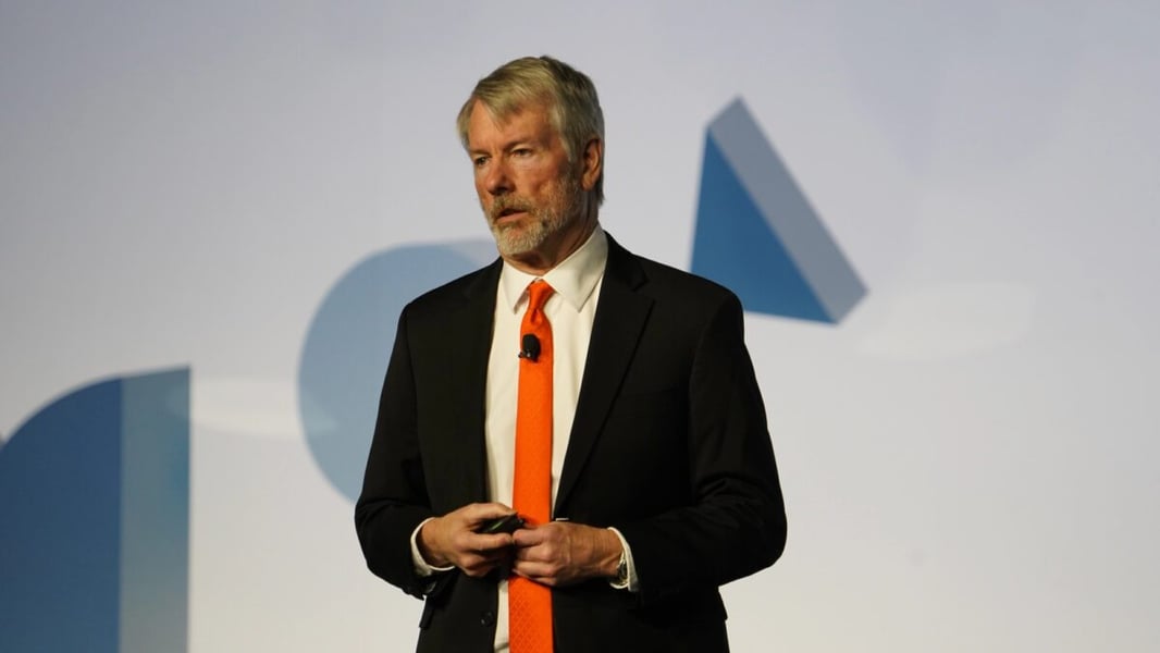 Strategy Executive Chairman Michael Saylor in a dark suit and orange tie speaking on stage