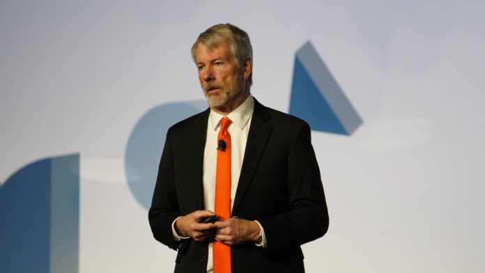 Strategy Executive Chairman Michael Saylor in a dark suit and orange tie speaking on stage