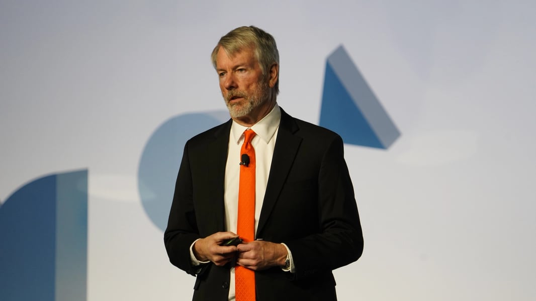 Strategy Executive Chairman Michael Saylor in a dark suit and orange tie speaking on stage