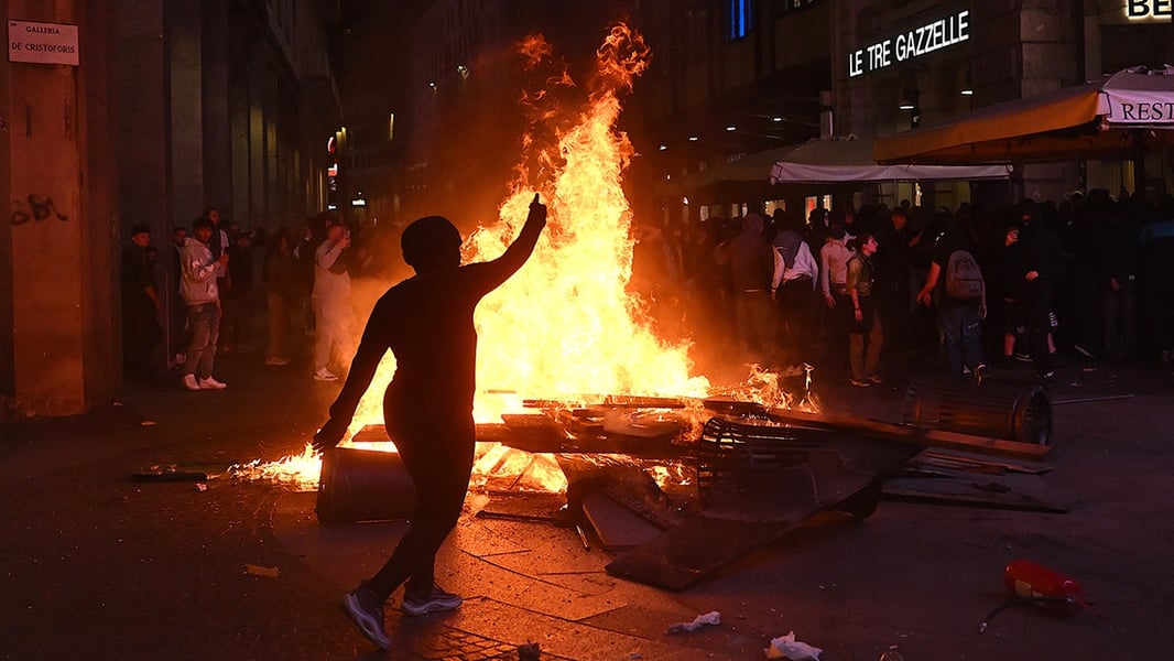 A protester raises an arm beside a burning barricade at night in central Milan during the cost-of-living protest