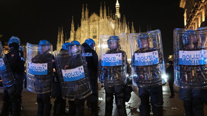 Riot police with shields lined up at night in front of the illuminated Milan cathedral during the October 17 protest