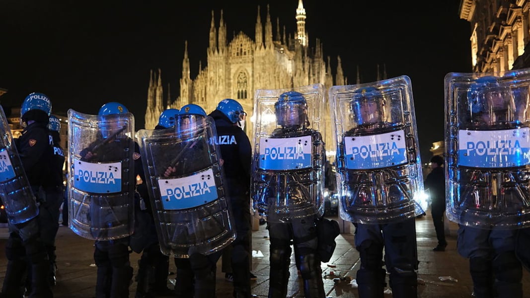 Riot police with shields lined up at night in front of the illuminated Milan cathedral during the October 17 protest