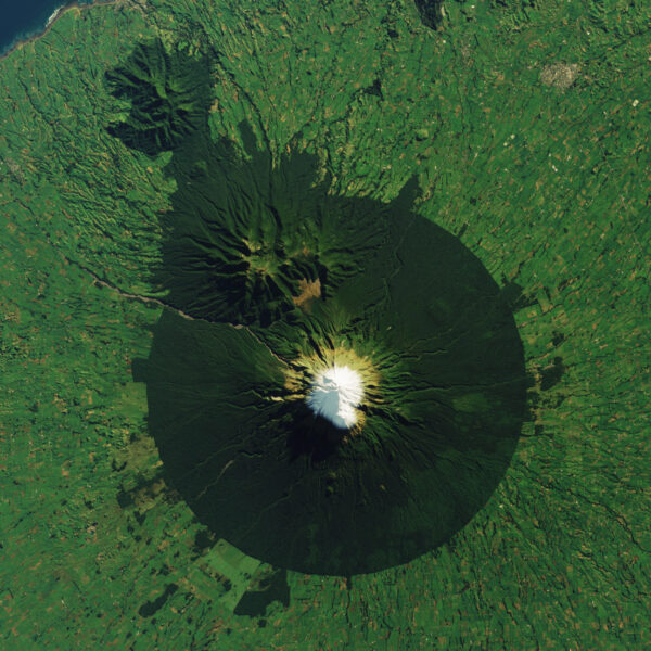 Landsat 8 satellite image of snow-capped Mount Taranaki in New Zealand ringed by dark forest inside a circular protected-area boundary, surrounded by green farmland